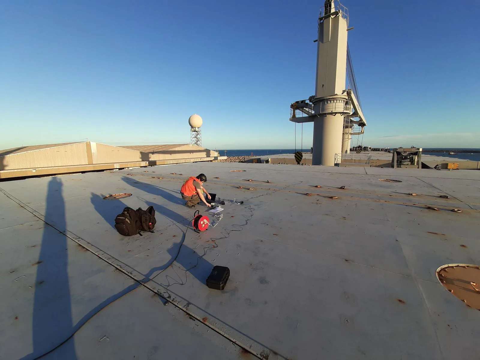 Engenheiro adquirindo dados no convés de um navio com o porto ao fundo