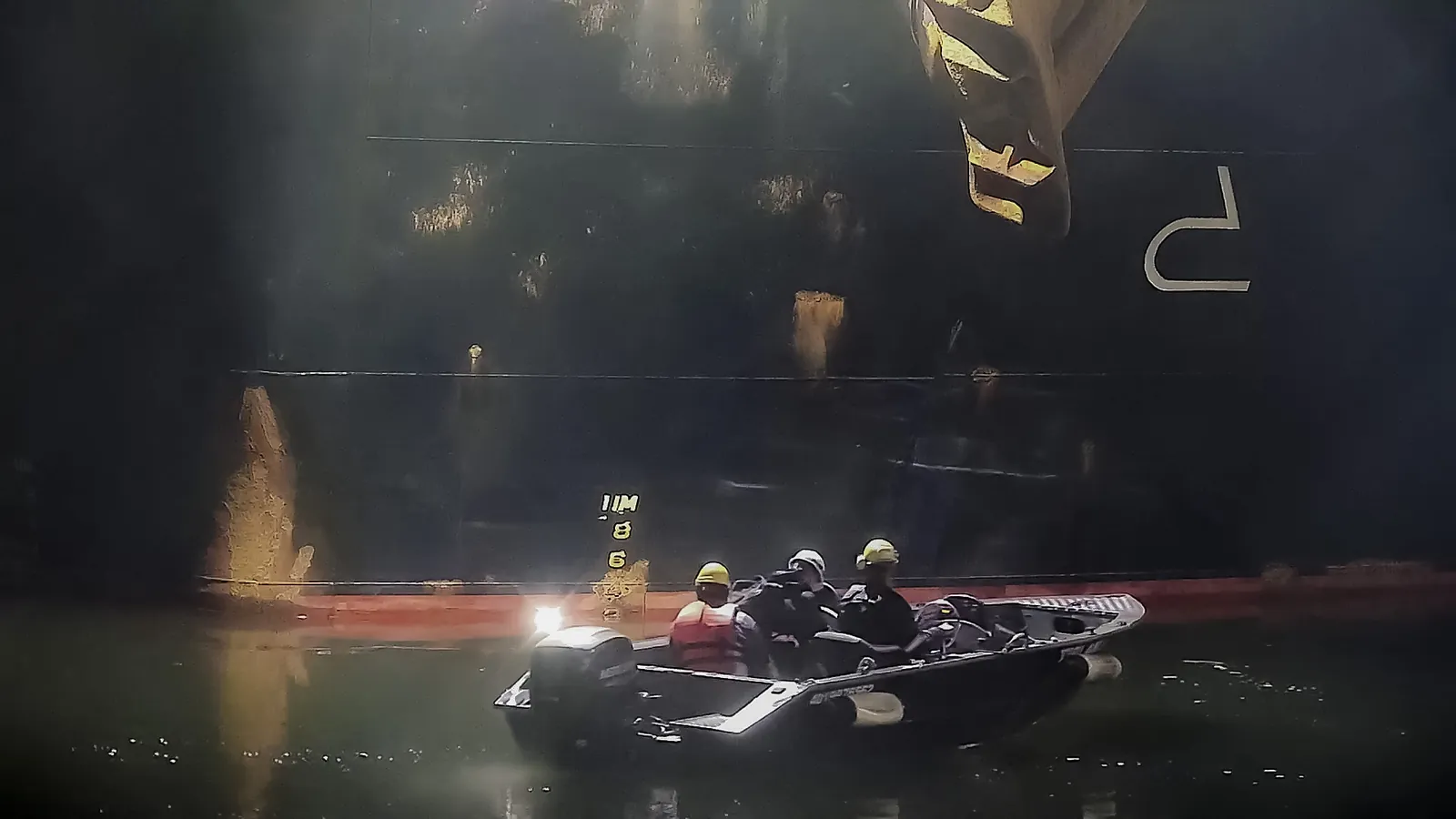 Equipe em uma lancha, à noite, lendo as marcas de calado no costado de um navio